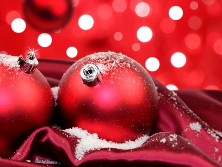 2 Red Christmas Balls Near Red Linen And White Snow With Red And White Bokeh Background