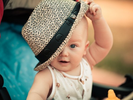 Baby In White And Brown Tank Top Holding Hat