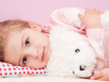 Smiling Girl Holding White Bear Plush Toy While Lying On Bed