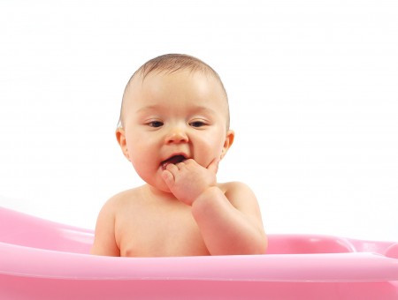Brunette Baby In A Pink Rubber Pool With His Hand In His Mouth