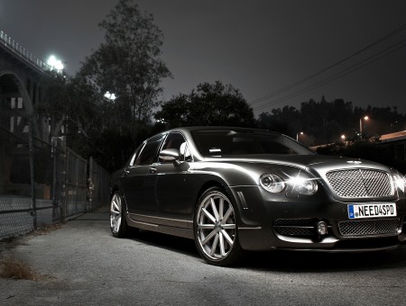 Black Luxury Sedan In Court Yard At Night With Trees And Houses In The Distance