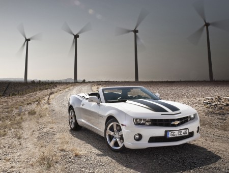White And Black Chevrolet Camaro Convertible On Dirt Road With 5 Windmills Turning In The Background During Daytime