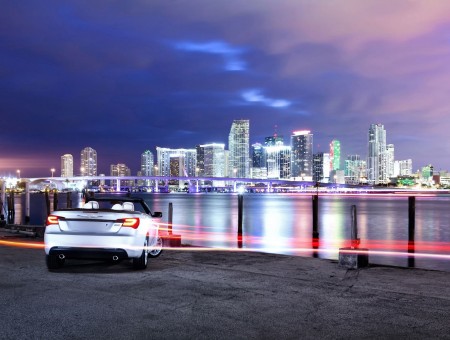 Silver Convertible Coupe In Dock With City Buildings In The Background During Night Time