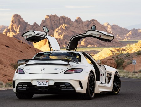White Mercedes Benz Sports Car Parked On Gray Asphalt Road Near Brown Rocky Mountain At Daytime