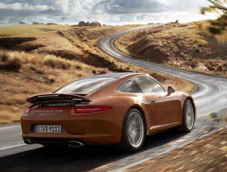 Brown Porsche 911 Turbo On A Valley Road Under A Gray Cloudy Sky