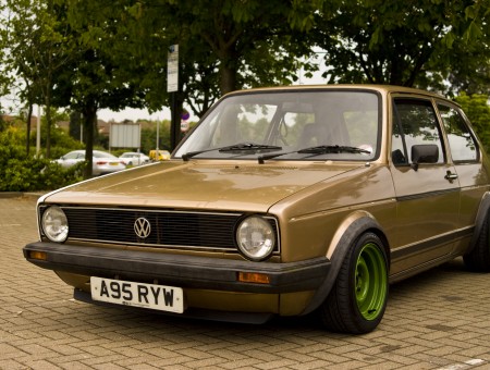 Brown Volkswagen Hatchback Car Parked On Parking Lot Surrounded With Green Trees During Daytime