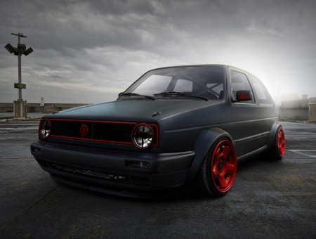Matte Grey And Red Volkswagen Golf Parked On Tarmac Under Grey Cloudy Sky
