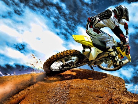 Man In White And Black Motorcycle Suit Riding Dirt Bike On Brown Rock Under Cloudy Sky