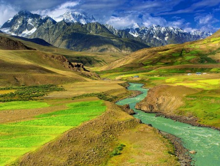 Small Canal River Flowing Between Open Field With Mountain Range In Background Under Blue Sky With White Clouds During Daytime