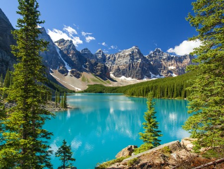 Rocky Mountain Cliff Surrounds The Green Forest With Clear Blue Calmed Water