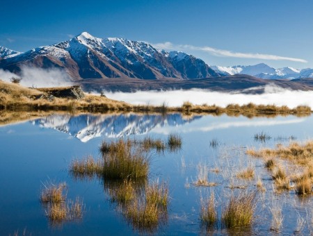 Brown Grass In Calm River With White Snow Covered Mountain Range Under Blue Sky During Daytime
