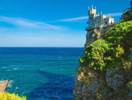 Castle On Cliff Beside Blue Body Of Water During Daytime