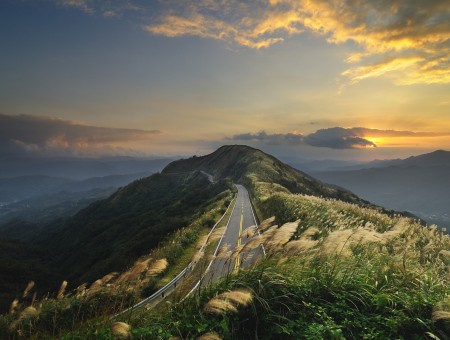 Road On Top Of The Green Mountains Under Cloudy Skies During Sunset