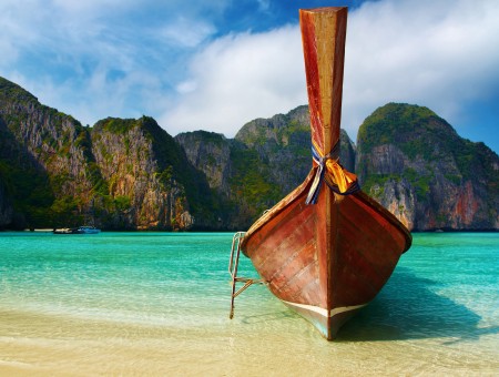 GREEN COVERED MOUNTAINS BEHIND A BOAT ON A BEACH SHORE