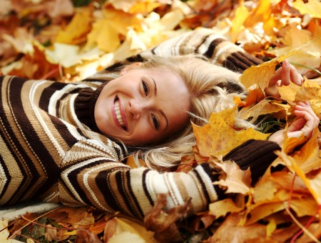 Woman In Beige And Brown Striped Sweater Lying On Maple Leaves Covered Surface