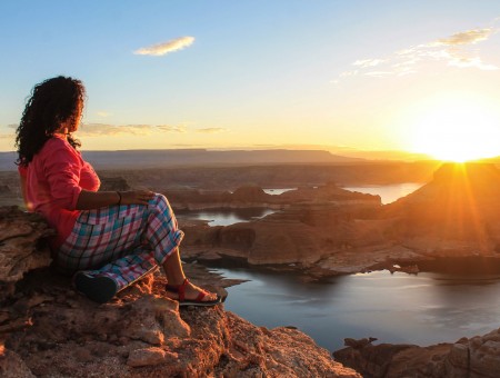 Woman Sitting On Rocky Mountain Overlooking River During Sunset