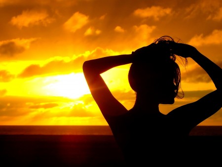 Silhouetted Woman Holding Her Hair Up In Front Of A Sunset