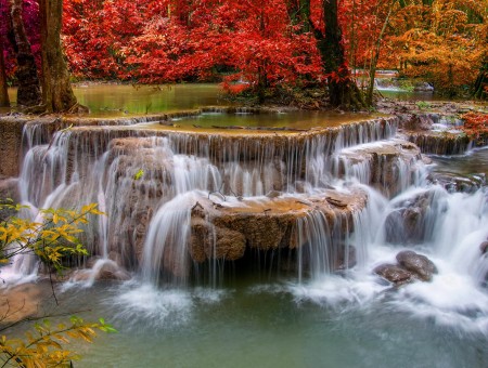 Low Waterfalls Over Brown Rocks By Red Trees