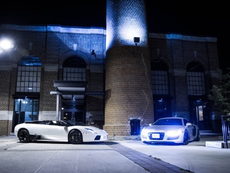 Two White Sports Cars Parked By Grey Brick Building