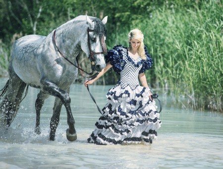 Woman In Blue Black And White Scoop Neck Puff Sleeve Gown Holding And Walking With Grey Horse In Body Of Water