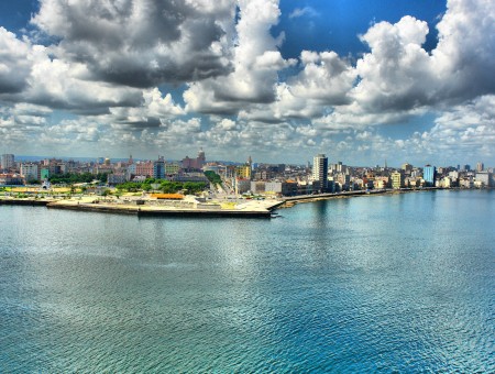 City Buildings Beside Blue Body Of Water Under Blue Sky And White Clouds During Daytime