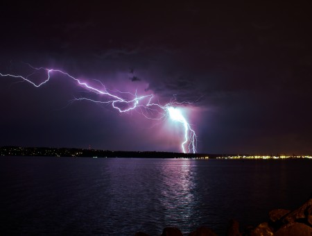 Lightning Striking Land Near Blue Body Of Water During Night Time