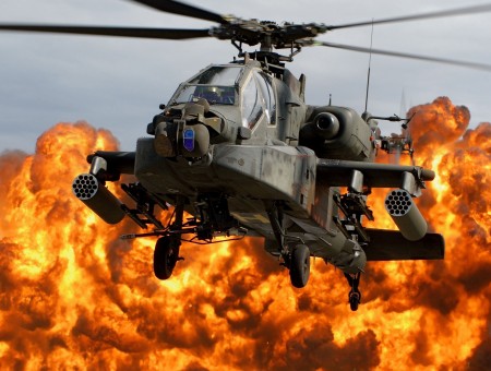 Gray Apache Helicopter Flying In The Air With Fire Explosion Behind During Daytime