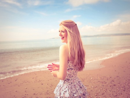 Smiling Blonde Haired Woman In White And Black Floral Dress On Ocean Shore