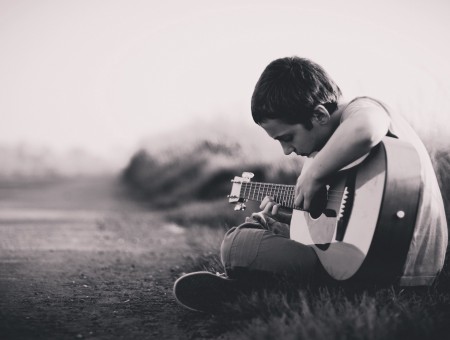 Grayscale Photography Of Boy Sitting On Grass While Playing Guitar
