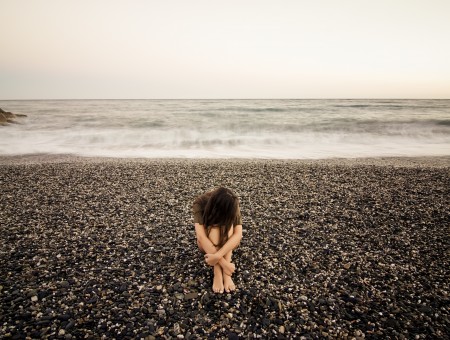 Woman Sitting On Sand Near Body Of Water